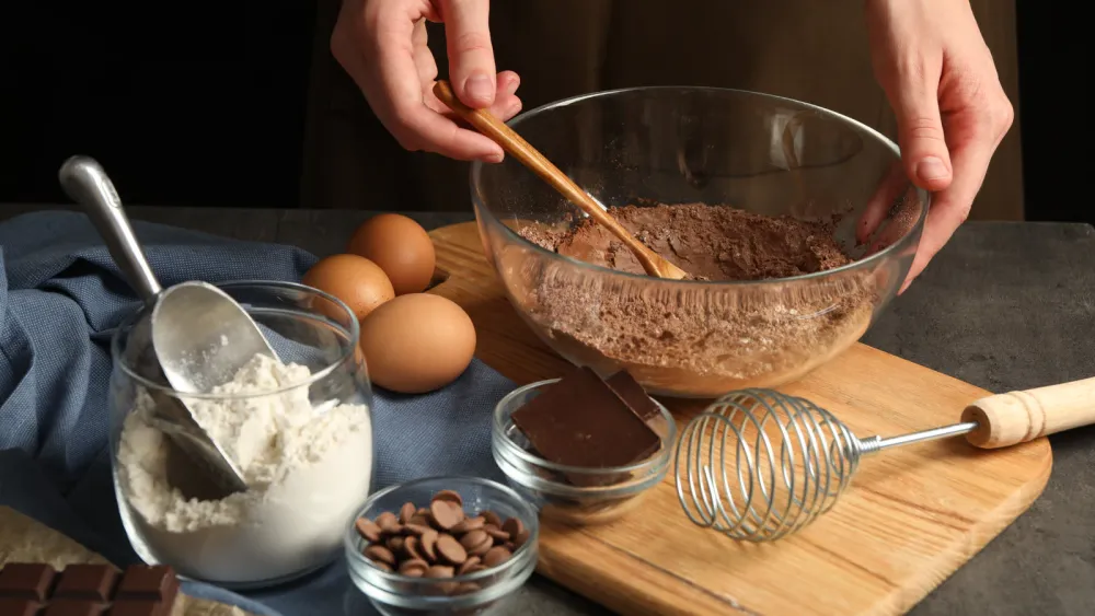 Mixing cocoa powder with flour, eggs, and chocolate in a glass bowl for baking